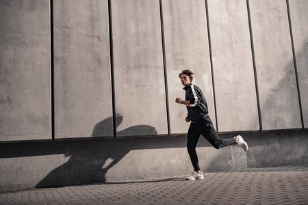 Young athlete is running near the stadium. Side viewの写真素材