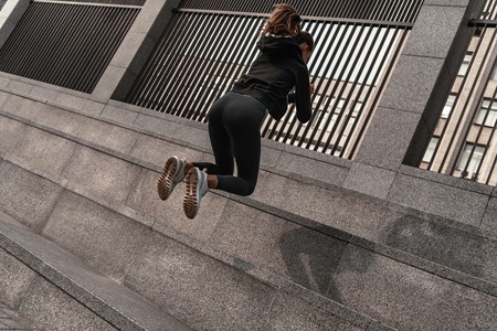 Young woman doing leg exercises with stone stairsの写真素材