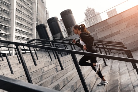 Sporty young woman is running upstairs outdoors. Side viewの写真素材