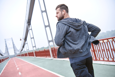 Morning workout. Close up of young man in sports clothing exercising while jogging on the bridge outdoorsの写真素材