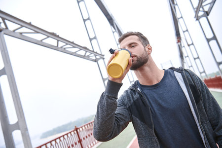 Tired after jogging. Young manin sports clothing bending and looking tired while standing on the bridge and urban view in the backgroundの写真素材