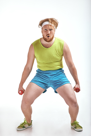Red haired, bearded, plump man is holding the dumbbellsの写真素材