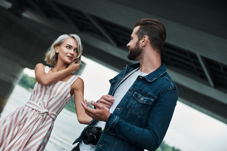 Romantic date outdoors. Young couple walking on the city street holding hands looking at each other joyful close-upの写真素材