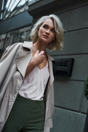 Fashion. Young stylish woman walking on the city street looking aside pensive close-upの写真素材