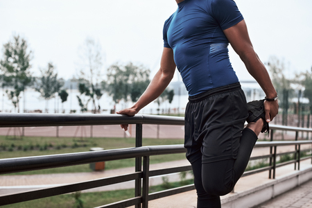 A close-up portrait of an african fitness man stretching legs on a national park background. Cropped photoの写真素材