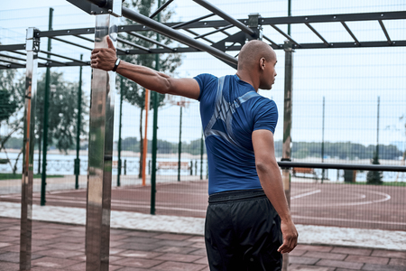 Rear view of an african sportive man who is stretching handsの写真素材