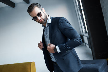 Young stylish businessman leader indoors at office wearing sunglasses looking aside thoughtfulの写真素材
