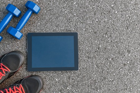 Smart sports gadgets. Cropped photo of dumbbells, water and black sneakersの写真素材