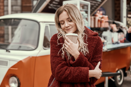 Beautiful woman with long hair sniffs coffee and huggs herself.の写真素材