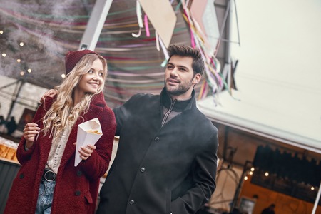 Close-up of young couple are eating french fries at the street food market.