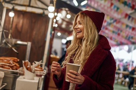 Happy stylish woman drinking mulled wine at the street food market.の写真素材