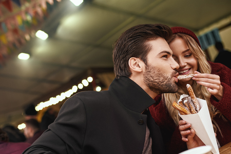 Close-up of young couple are eating churros at the street food market.の写真素材