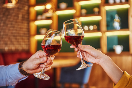 Two glasses together. Close-up of couple holding red wine in restaurantの写真素材