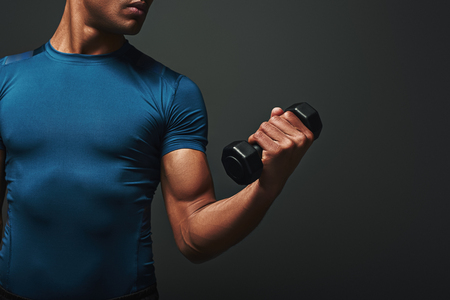 Stronger, Better, Faster. Dark skinned sportsman working out with dumbbells over dark backgroundの写真素材