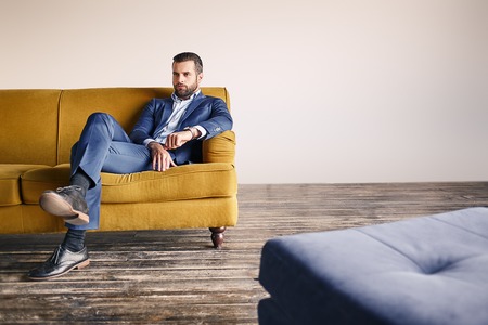 Confident businessman. Young and attractive bearded man dressed in fashionable suit is relaxing on...