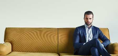 Waiting for a meeting...Well-dressed young and successful businessman is sitting on sofa at office and waiting somebodyの写真素材