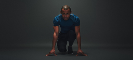 At the start! Young sportsman is ready to run standing over dark backgroundの写真素材