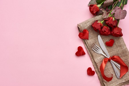 Romantic dinner. Close up of table setting with fresh red roses and decorative hearts