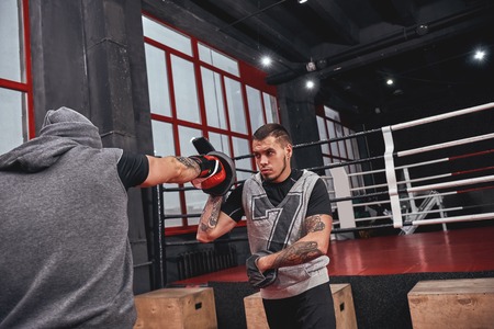 Training his boxing skills. Muscular athlete in red gloves training on boxing paws with partner in boxing gymの写真素材