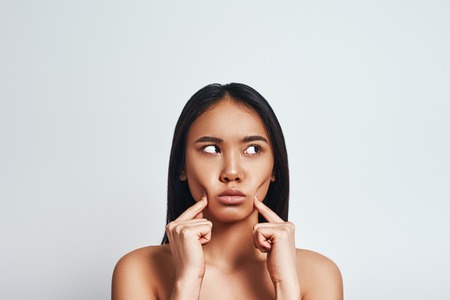 Upset young asian woman looking away and making a sad face while standing on a grey background.の写真素材
