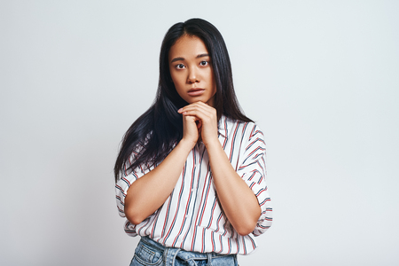Studio shot of charming young asian female with natural beauty looking calmly at camera, isolated over grey background.の写真素材