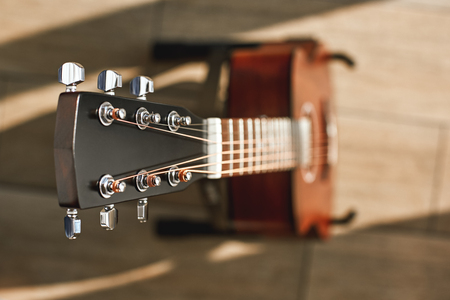 Beauty of musical instrument. Creative top view photo of the brown acoustic guitar with focus on the headstock against the wooden floor.の写真素材