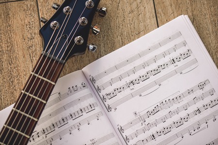 Playing guitar... Close-up photo of guitar neck and music notes against of wooden background.の写真素材