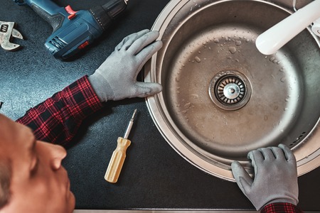 Inside view. Close-up of handsome plumber repairing sink in kitchenの写真素材