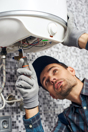 Set up boiler. Worker set up electric heating boiler at home bathroomの写真素材