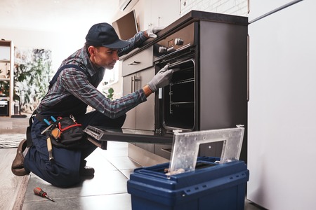 Dont delay with repair. Close-up of repairman examining ovenの写真素材