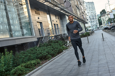 Morning workout. Young and strong african man in stylish sportswear running in the cityの写真素材