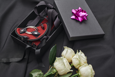 Valentine's Day gift ideas. Close up photo of a gift box with bdsm stuff and fresh white roses laying on a black silk. Erotic toys. Gifts for adultsの写真素材