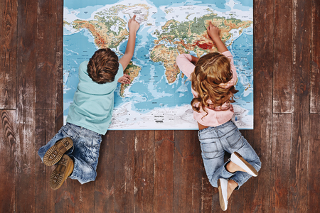 Discover the World. Children lying on world map, looking at itの写真素材