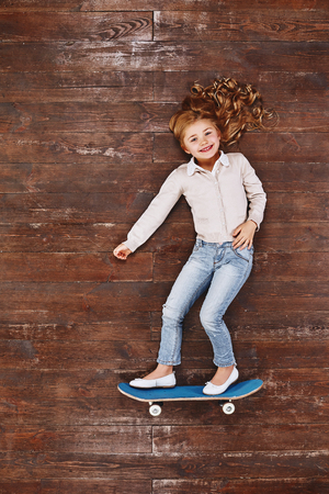 Its fun being a kid. Girl on a skateboard, lying on the floor, looking at camera and smilingの写真素材