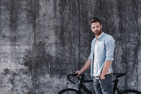 Nothing compares to the simple pleasure of riding a bike. Handsome brown-haired man with blue eyes standing with a bicycle isolated over grey backgroundの写真素材
