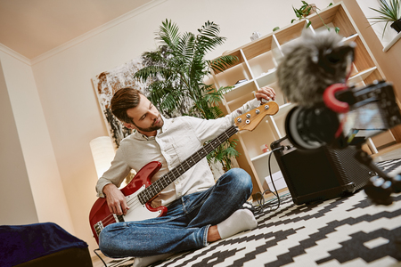 Preparing instrument. Handsome male music blogger adjusting electric guitar for recording new video lessonの写真素材