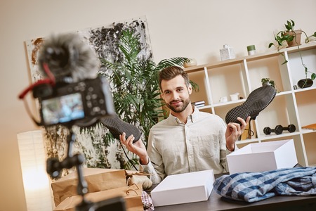 Fashion advice. Smiling male fashion blogger showing sport shoes on camera while recording new video for his fashion blog.の写真素材