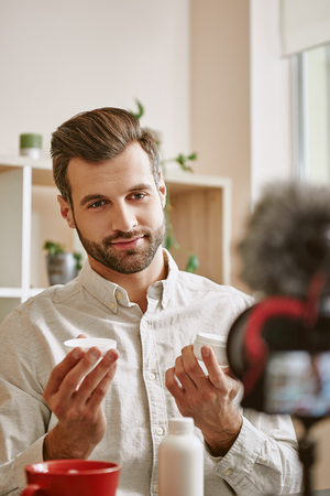 Skincare for men. Vertical photo of positive and young male blogger showing new cosmetic product on camera while live streamingの写真素材