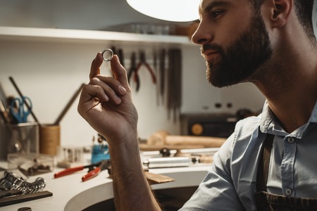 My precious. Close up of young male jeweler looking and inspecting a ring.の写真素材