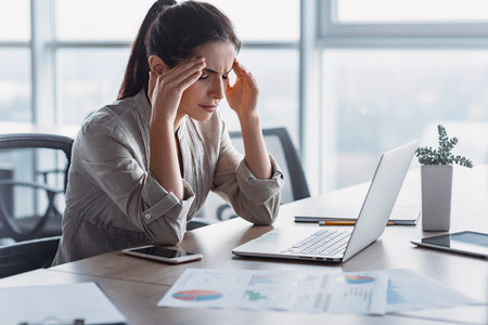 Young attractive woman at modern office desk. She has severe headache. Office syndrome conceptの写真素材