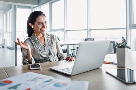 Smiling businesswoman wearing headphones, listening to music, posing at workplace