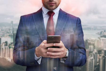 Chat with client. Close up portrait of businessman hands using smart phone while standing against of modern office buildings. Digital. Technologiesの写真素材