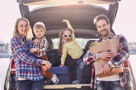 Every day we make deposits in the memory banks of our children. Family stands near the car, looking at camera and smiling. Family road tripの写真素材