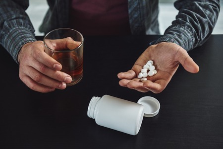 You largely constructed your depression. It wasnt given to you. Therefore, you can deconstruct it. Close up of man sitting at table with alcohol and drugs. Alcoholism conceptの写真素材