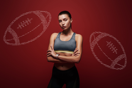 Young sportswoman standing with her arms crossed over red background.の写真素材