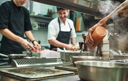 Professional team. Cheerful young cooks preparing food together in a restaurant kitchenの写真素材