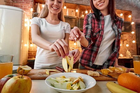 Good food. Good friends. Good times. Young female friends preparing together healthy meal in modern kitchen. Cozy interiorの写真素材