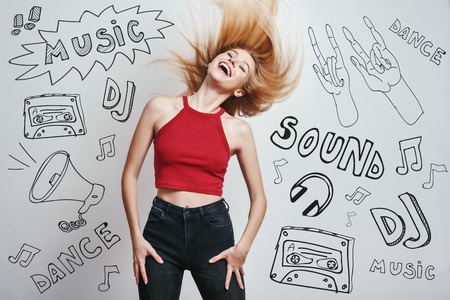 Feeling the freedom. Elegant and charming woman with long blond hair keeping eyes closed and smiling while standing against grey background with music theme doodles. Music concept. Partyの写真素材