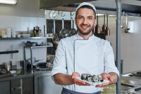 Speak with the taste. Portrait of cheerful chef standing with cooked traditional japanese sushiの写真素材