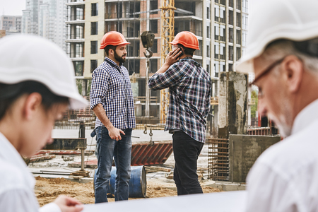 Busy day. Team of professional engineers and builders in protective wear are working together at...